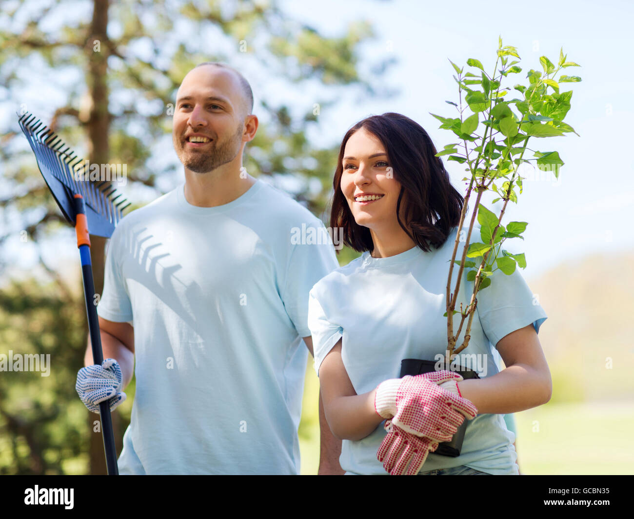 Freiwillige paar mit Bäumen und Harke im park Stockfoto