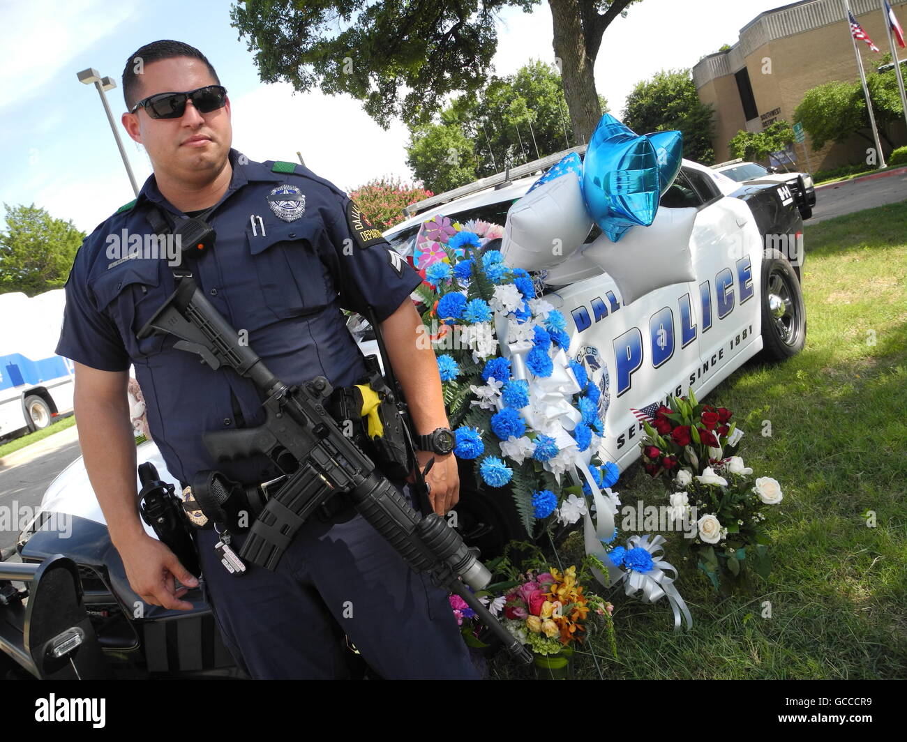 Texas, USA. 8. Juli 2016. Ein US-Polizist steht neben einem Polizeiauto bedeckt in Blumen vor einer Polizeistation in Dallas, wo einige der Polizisten wirkte, die erschossen oder verwundet am Vorabend in Texas, uns, 8. Juli 2016. Ein Scharfschütze hatte fünf Polizisten angeschossen und verletzt mehrere weitere in Dallas. Foto: Johannes Schmitt-Tegge/Dpa/Alamy Live News Stockfoto