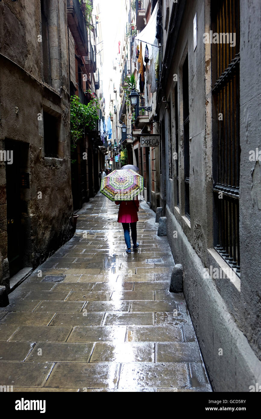 Eine Frau Walkiing auf einer schmalen Barcelona Straße während ein leichter Regen sportlichen einen Barcelona-Schirm. Stockfoto