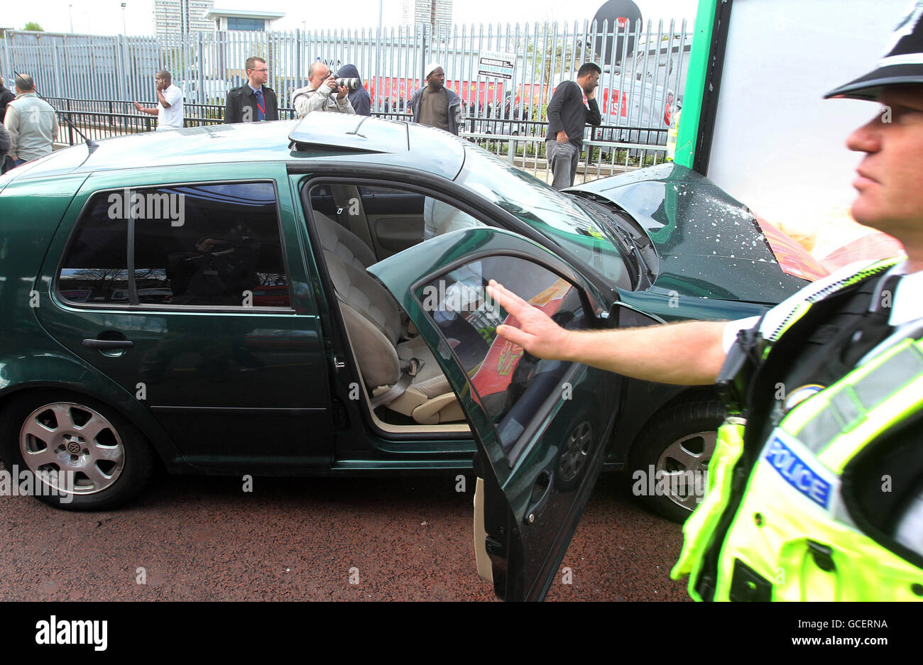 Ein Polizeibeamter steht neben dem Auto, das während des Starts der neuesten Kampagnenplakate des Premierministers der Labour-Partei in Birmingham in eine Busunterkunft stürzte, die über das Geländer hinaus sichtbar sind. Stockfoto