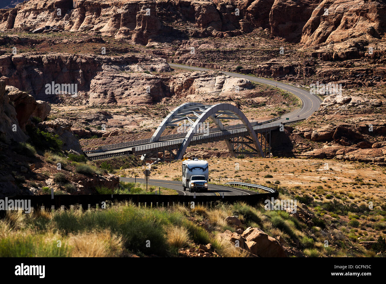 LKW ziehen einem RV Camper auf einer kurvenreichen Straße durch Canyon Land mit einer modernen, Stahl-Brücke im Hintergrund; Utah, USA Stockfoto