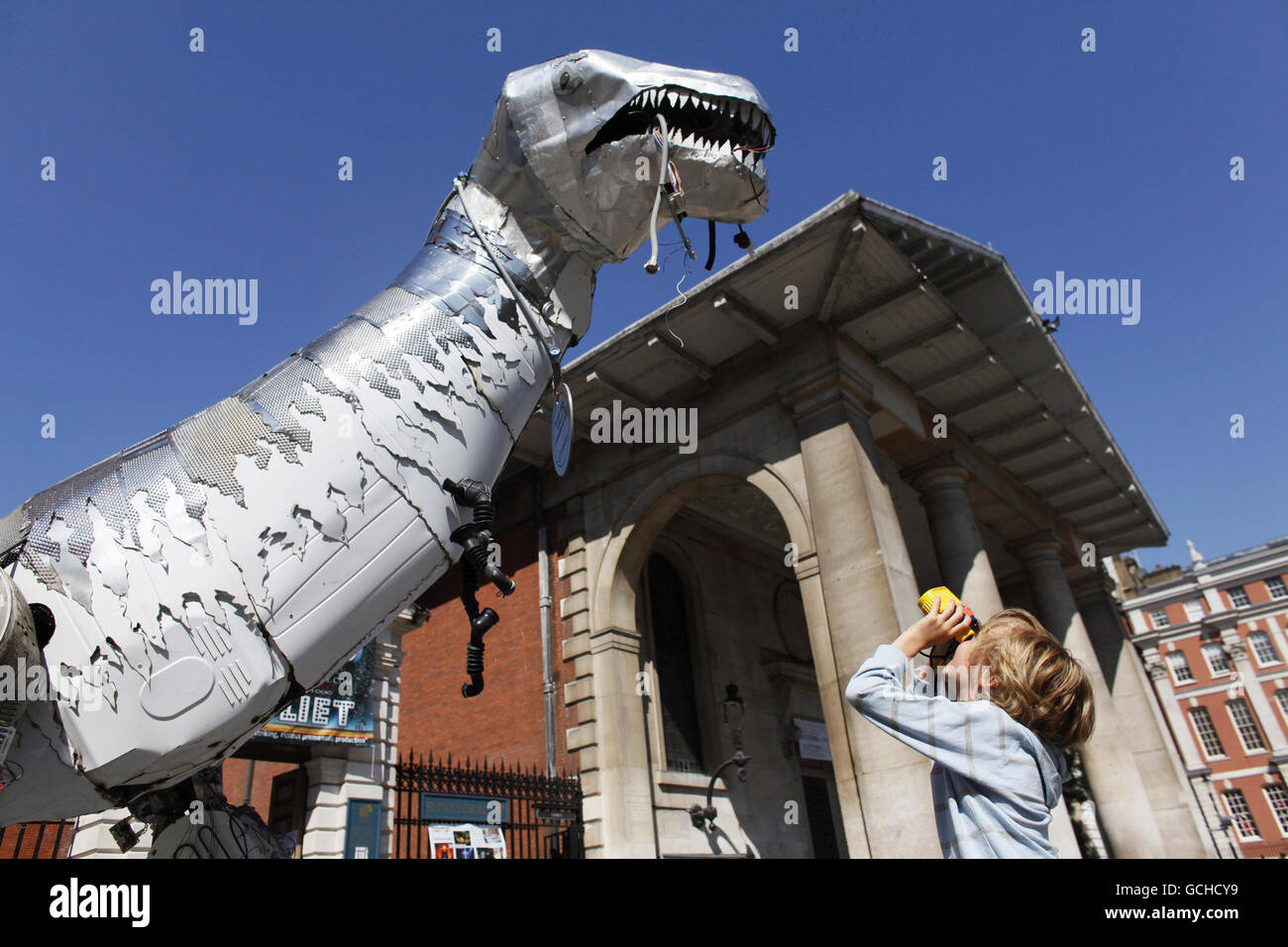 Leon Depreli blickt durch sein Fernglas auf „Tyrone the Recycled Rex“, eine 4 Meter hohe Dinosaurier-Skulptur, die vollständig aus recycelten Haushaltsgeräten hergestellt wurde, während sie im Londoner Covent Garden von der Indesit Company UK anlässlich des Starts der Recycle Week (21-27. Juni 2010) losgelassen wird. Stockfoto