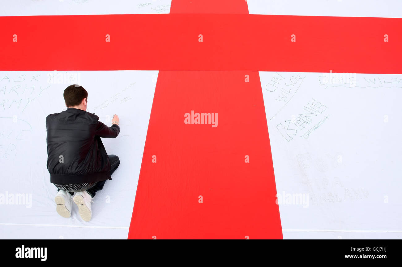 Ein Mann schreibt eine Unterstützungsbotschaft für die englische Fußballmannschaft auf einer riesigen Saint George's Cross-Flagge auf dem Trafalgar Square im Zentrum von London vor dem Weltcup-Spiel gegen Algerien heute Abend Stockfoto