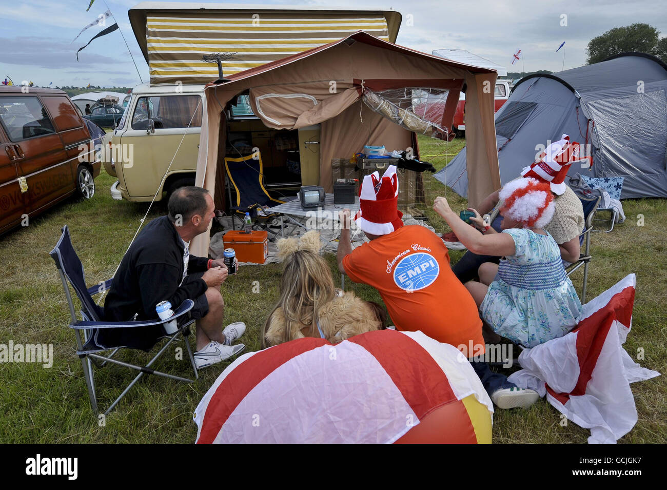 England-Fans versammeln sich um einen kleinen, tragbaren Schwarz-Weiß-Fernseher, der mit einer Autobatterie verbunden ist, während sie das Fußballweltcup-Spiel England gegen USA auf einem Campingplatz im Bristol Volksfest VW-Festival sehen. Stockfoto