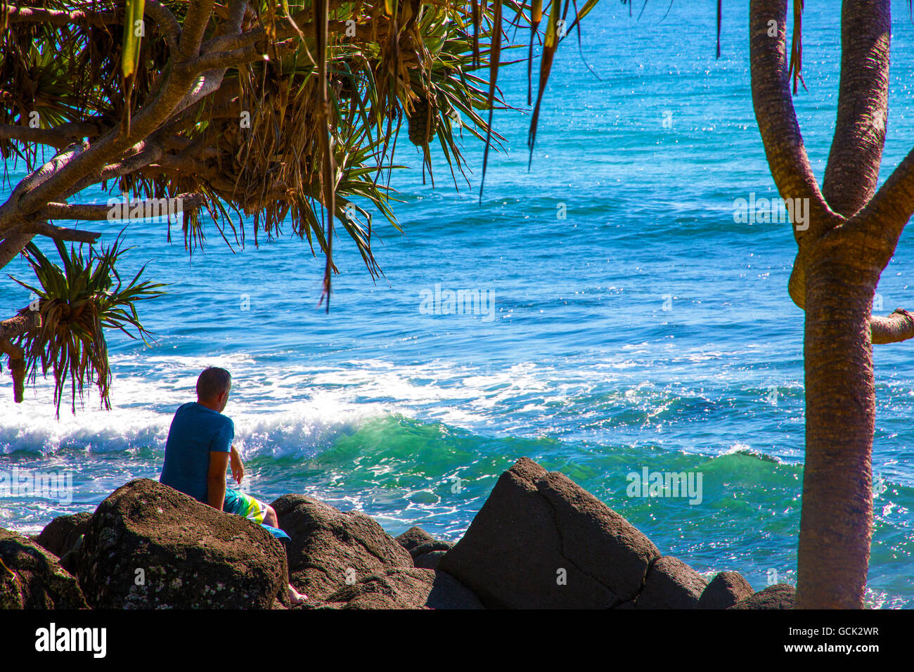 Mann sitzt auf den Felsen, Blick auf den Pazifischen Ozean in Burleigh Heads, Australien Stockfoto