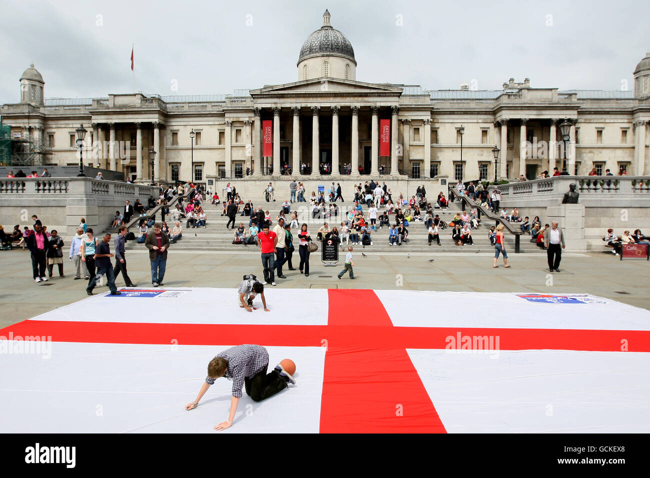 Ein Mann schreibt vor dem WM-Spiel gegen Algerien eine Unterstützungsbotschaft für die englische Fußballmannschaft auf einer riesigen Flagge des Saint George's Cross auf dem Trafalgar Square im Zentrum von London Stockfoto