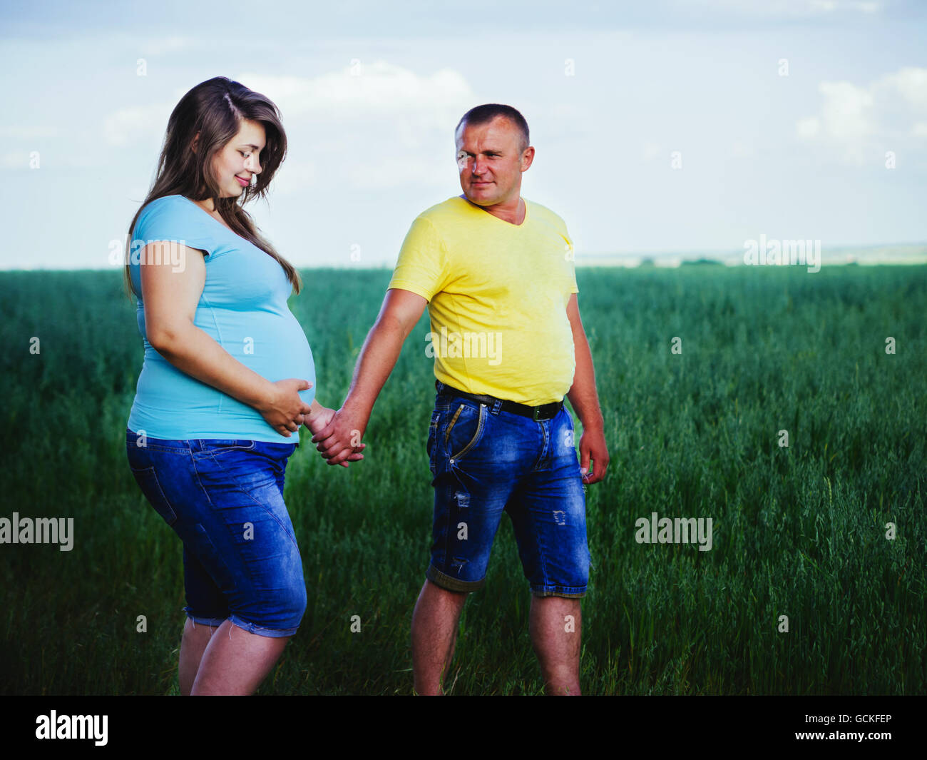 Schöne schwangere Frau mit Mann zu Fuß auf der Wiese Stockfoto