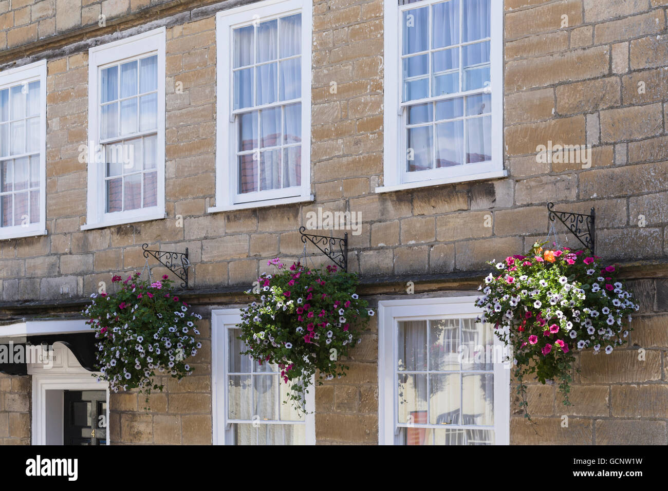 Bunte Blüten in hängenden Körben und Schiebefenster in Wotton-unter-Kante, South Gloucestershire. Stockfoto