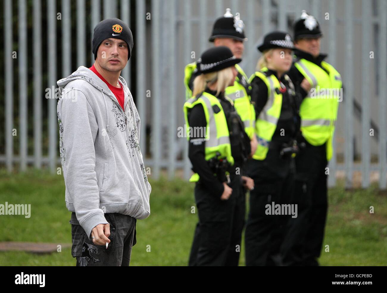 Ein Fan von Manchester United raucht vor dem Anpfiff vor dem Glanford Park unter den wachsamen Augen der Polizei eine Zigarette Stockfoto