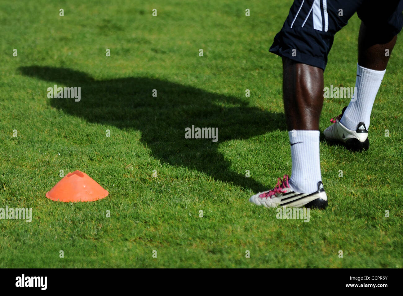 Allgemeine Ansicht eines Fußballers mit einem Paar adidas Fußballschuhe werfen einen Schatten, wie er um einen läuft Trainingskonus Stockfoto