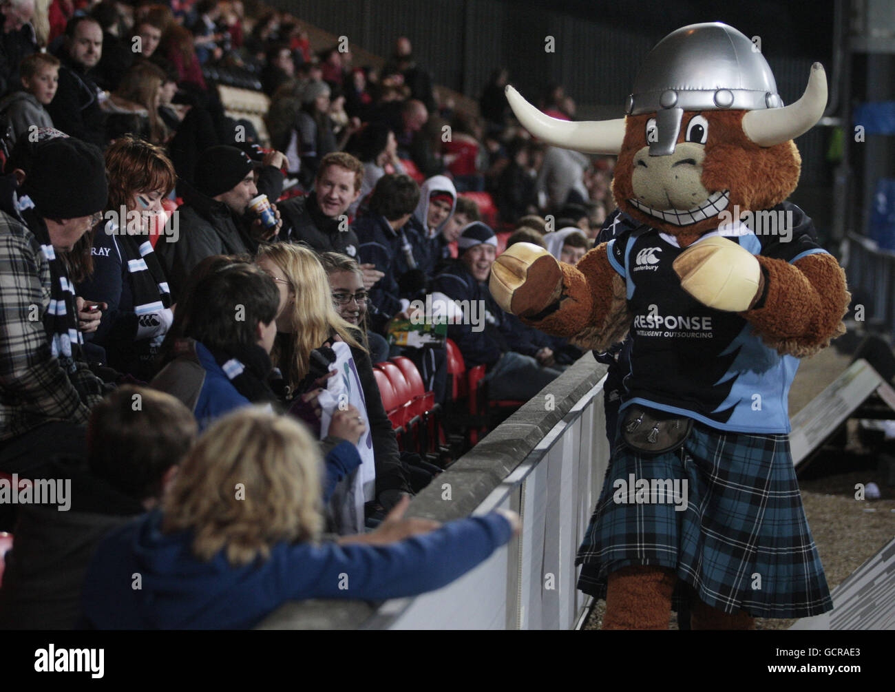 Rugby Union - Heineken Cup - Pool 6 - Glasgow Warriors gegen Newport-Gwent Dragons - Firhill Arena. Das Maskottchen der Glasgow Warriors, Clyde Cow, begrüßt junge Fans auf den Tribünen während des Heineken Cup, Pool 6-Spiels in der Firhill Arena, Glasgow. Stockfoto