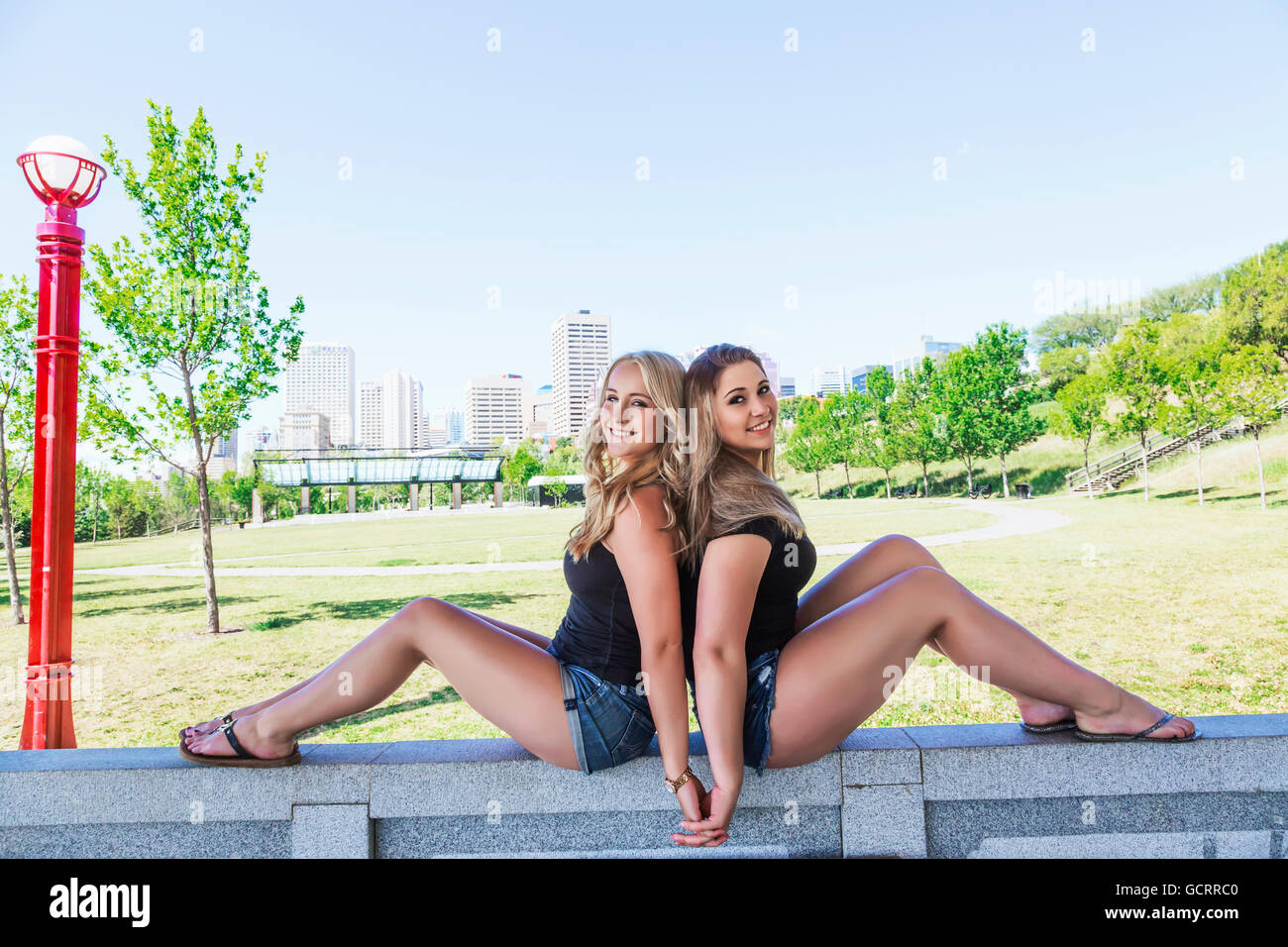 Zwei Freundinnen posieren für die Kamera und Hand in Hand an der Wand und genießen Sie die Natur in einem Innenstadt-Park; Edmonton, Alberta, Kanada Stockfoto