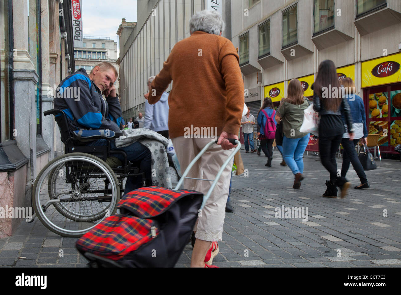 Hilfe für den obdachlosen, behinderten Bettler, der im Rollstuhl sitzt und von einem Passanten in Liverpool, Merseyside, Großbritannien, eine Geldspende erhalten hat Stockfoto