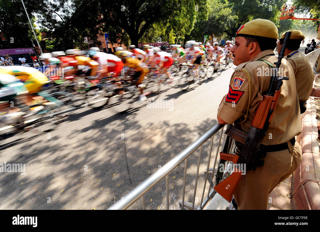 Das Hauptfeld passiert bewaffnete Sicherheit während des 168 km langen Men's Road Race am 7. Tag der Commonwealth Games 2010 in New Dehli, Indien. Stockfoto