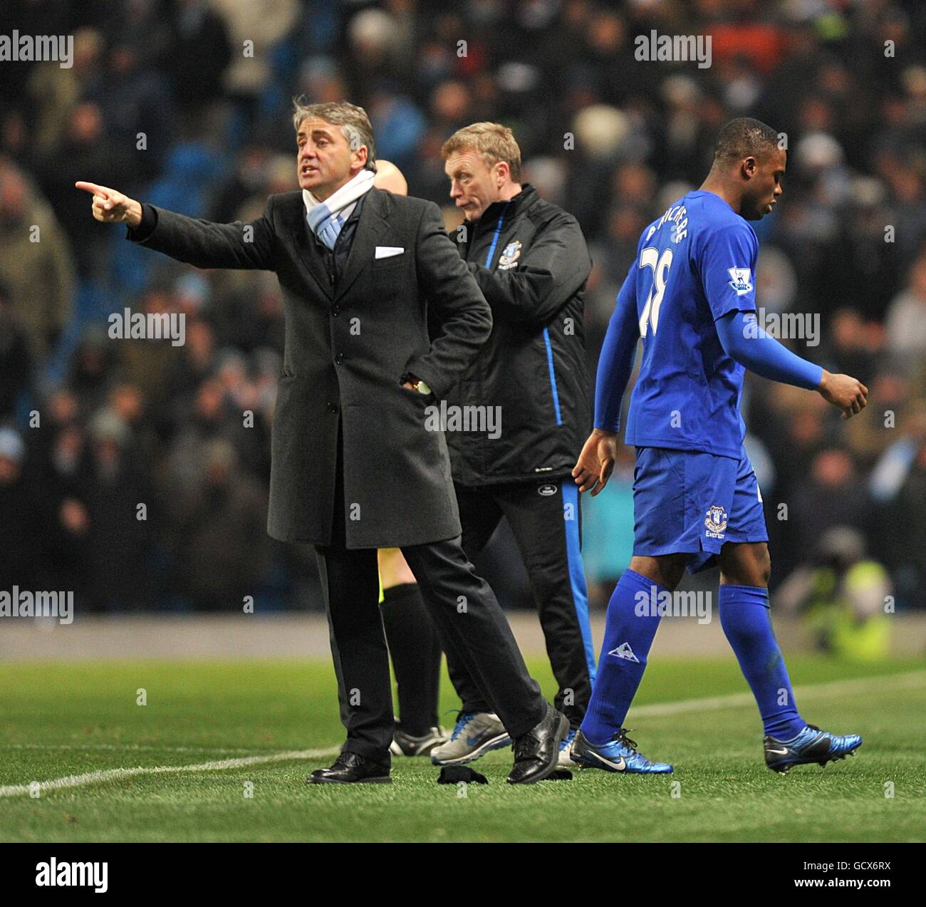 Everton-Manager David Moyes (Mitte) sieht zu, wie sein Spieler Victor Anichebe (rechts) abgeschickt wird, und Manchester City-Manager Roberto Mancini (links) gibt Anweisungen an sein eigenes Team. Stockfoto