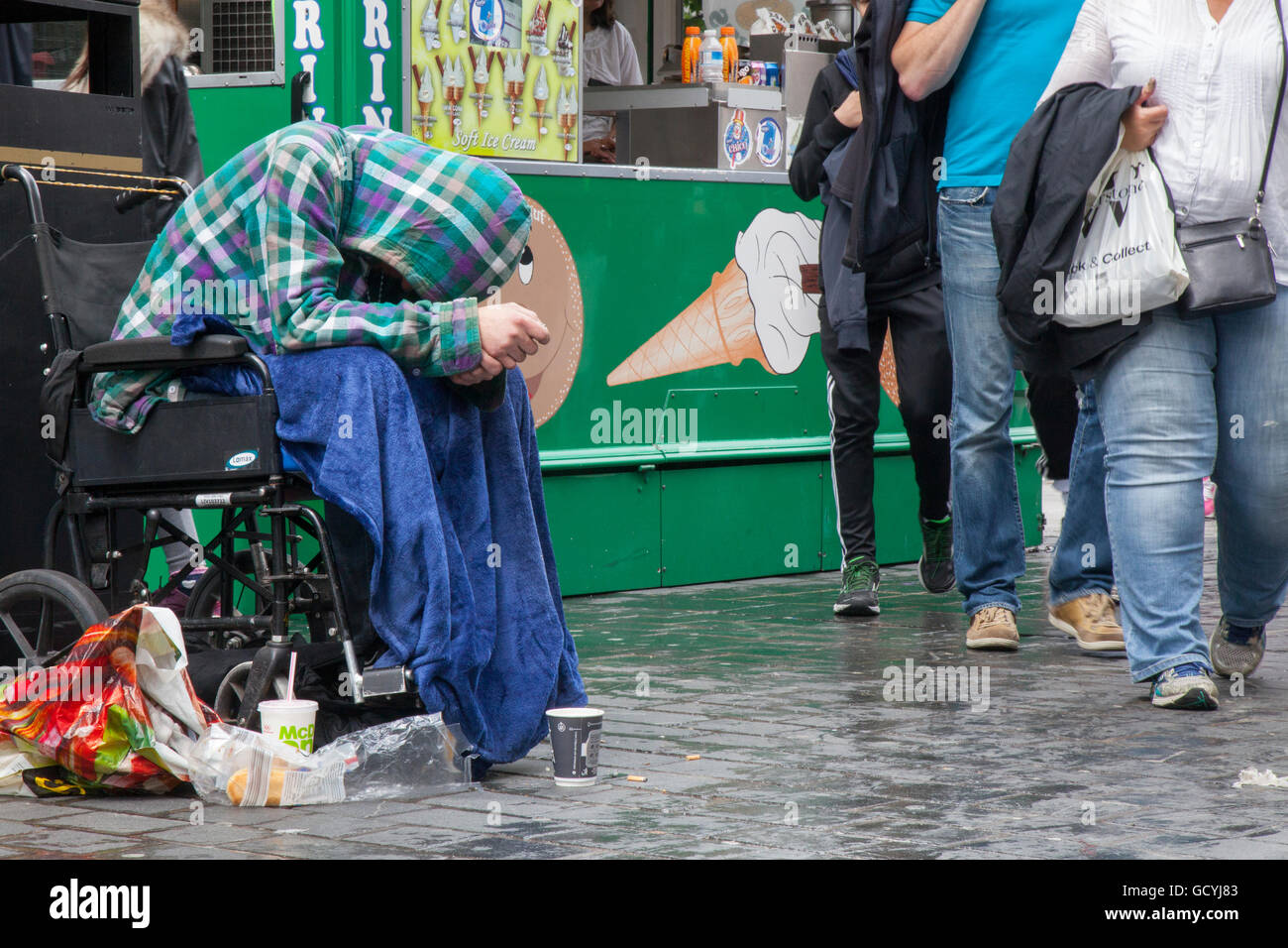 Menschen & Passanten vorbei gehen Behinderte obdachlose Bettler in einem Rollstuhl auf den Straßen von Liverpool, Merseyside, UK Stockfoto