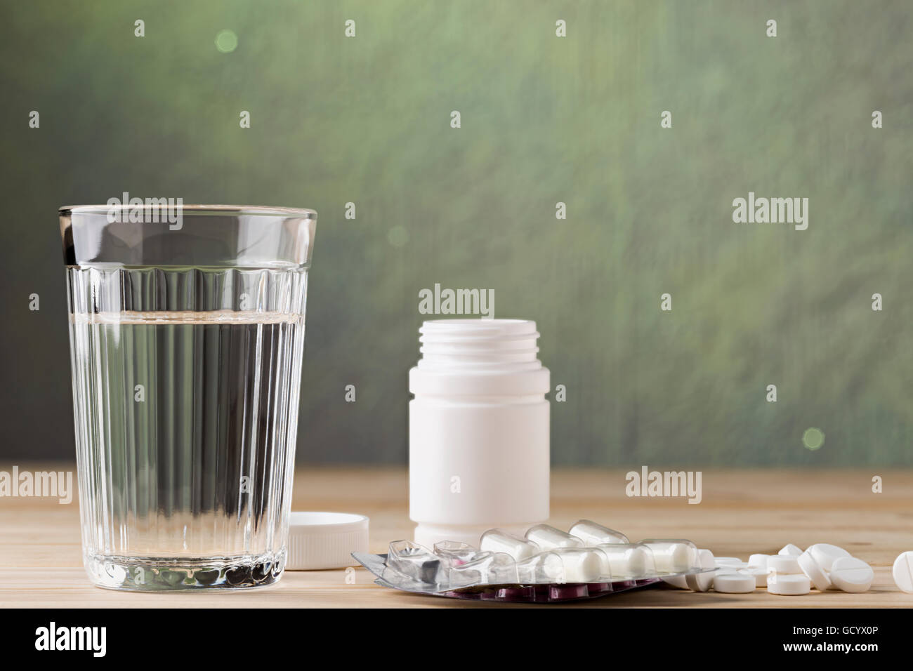 Glas von sauberen Wasser und Pille-Blister-Verpackungen auf Holztisch Stockfoto