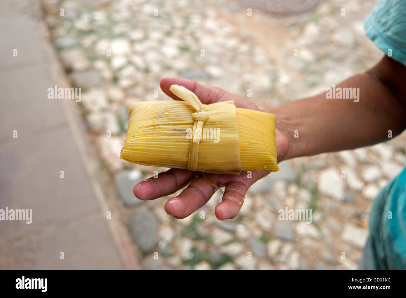 Ein kubanische Mann hält einen gedämpften Tamales Snack in der Hand mit Straße Kopfsteinpflaster im Hintergrund in Trinidad Kuba Stockfoto