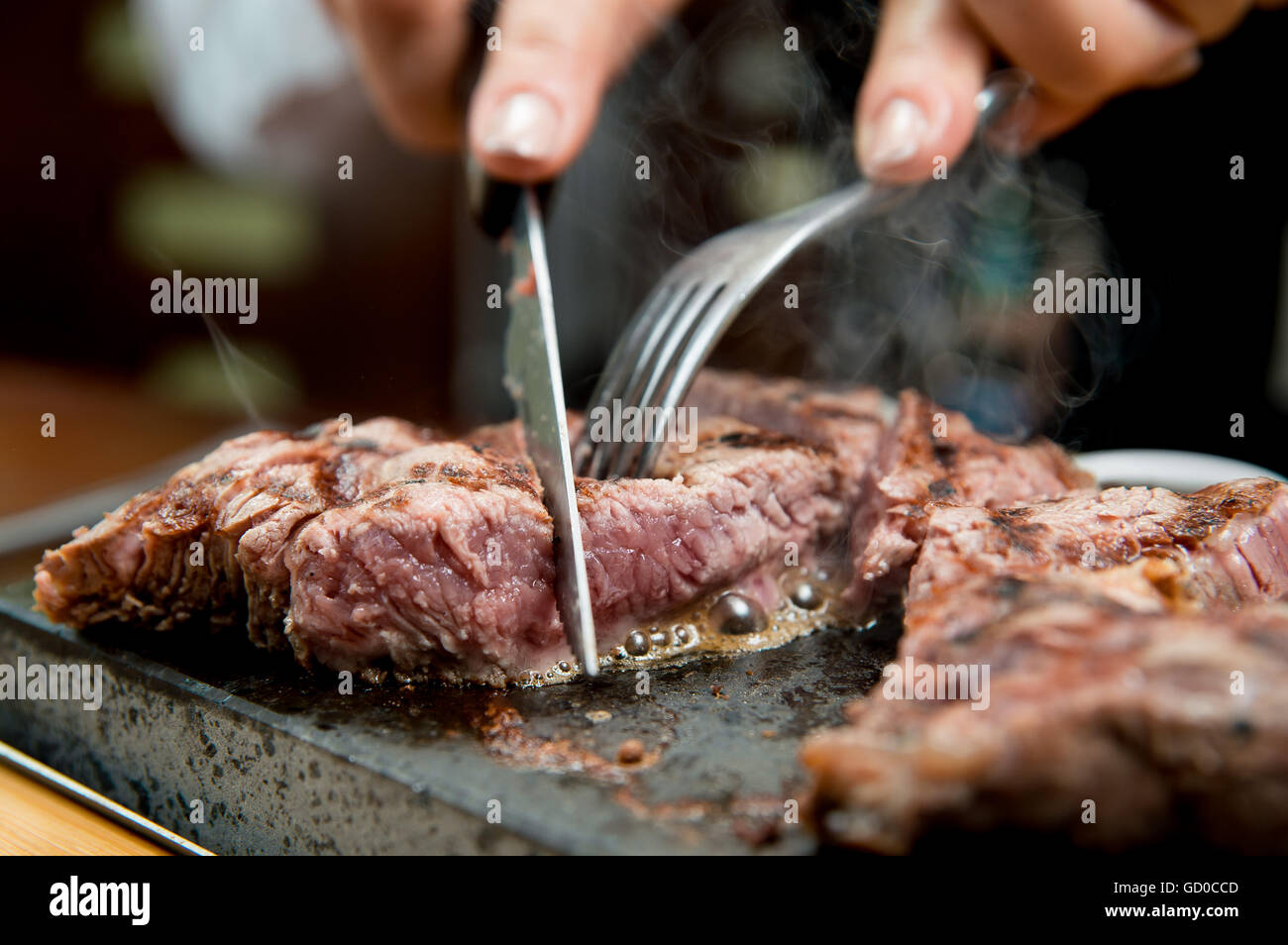 Ribeye Steak kochen bis zum Kunden Geschmack auf einem heißen Stein serviert mit Saucen, Pommes Frites und Salat. Stockfoto