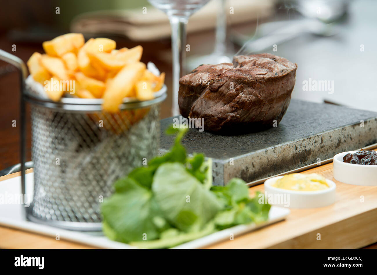 Filetsteak kochen bis zum Kunden Geschmack auf einem heißen Stein serviert mit Saucen, Pommes Frites und Salat. Stockfoto