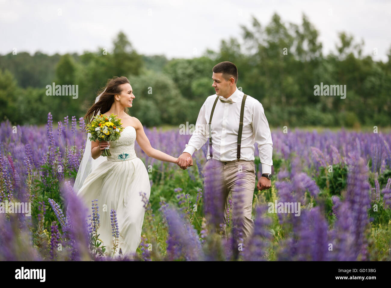 Glückliches Hochzeitspaar zu Fuß auf dem lupine Feld Stockfoto