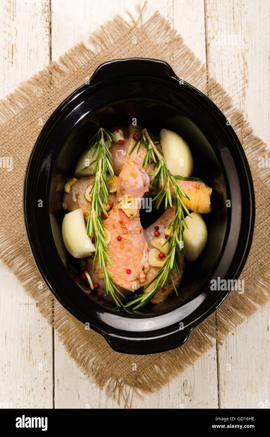 marinierte Hühnerbein mit Paprika, Zwiebeln, Knoblauch und Rosmarin in einem schwarzen slow cooker Stockfoto