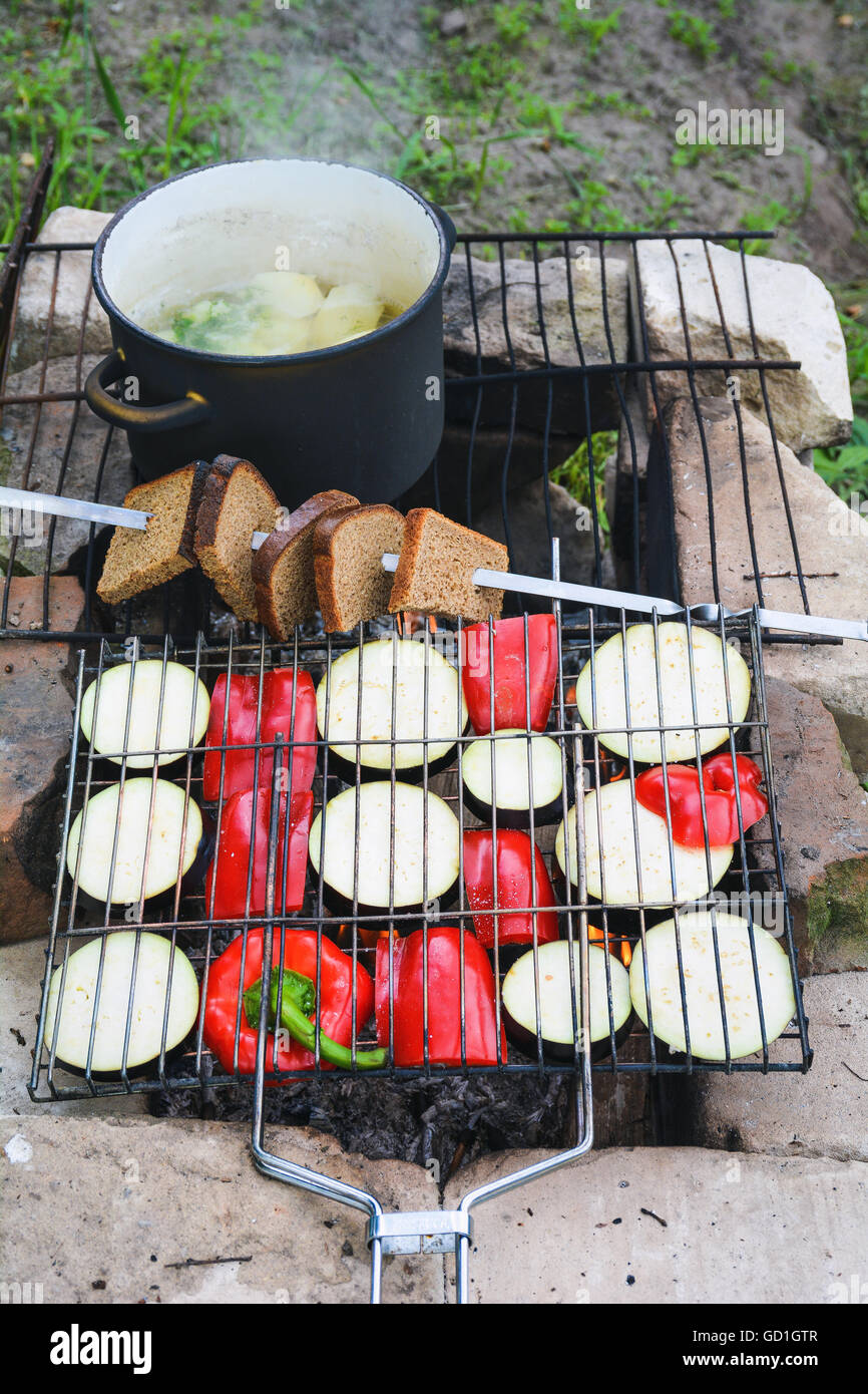 Am Lagerfeuer kochen. Gegrilltes Gemüse, geröstetem Brot und eine heiße Suppe Kochen am Feuer Stockfoto