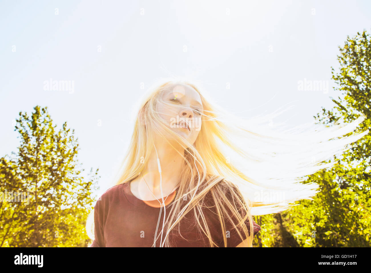 Schöne junge Frau, Musik hören und mitsingen beim Schwingen ihr langes, blondes Haar im Freien in einem Stadtpark; Edmonton, Alberta, Kanada Stockfoto