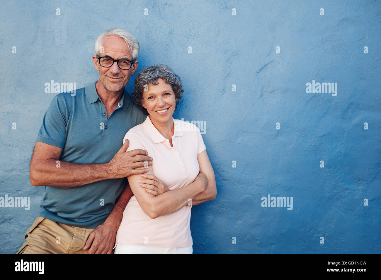 Porträt von glücklich älteres paar zusammenstehen gegen blaue Wand. Mitte im Alter von Mann und Frau, Blick in die Kamera und lächelnd auf Stockfoto