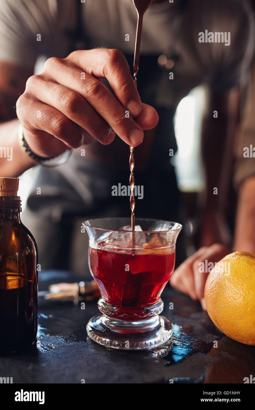 Closeup Aufnahme der Barkeeper Hand rühren Negroni Cocktail. Glas des Getränks auf Theke mit Grapefruit und Sirup Flasche. Stockfoto