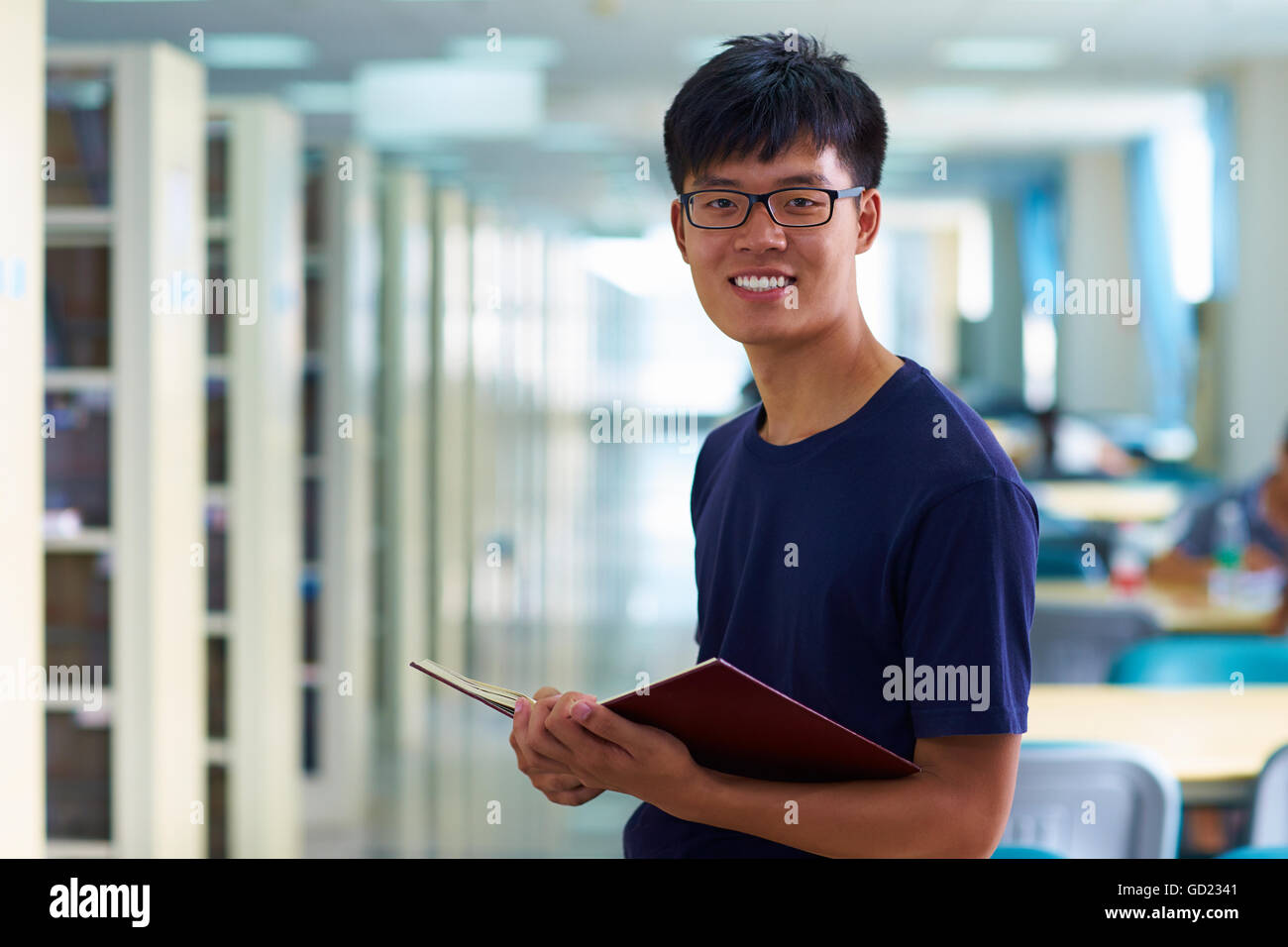 Eine junge männliche asiatische und chinesische Studenten Blick auf Kamera Lächeln in der Bibliothek Stockfoto