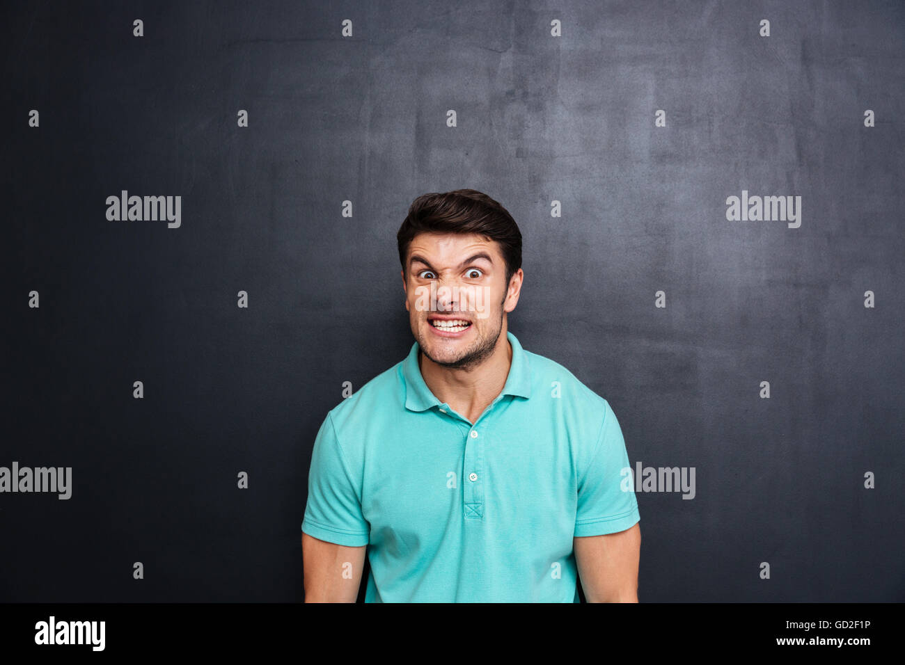 Verrückte aggressive junge Mann im blauen T-shirt über Blackboard Hintergrund Stockfoto