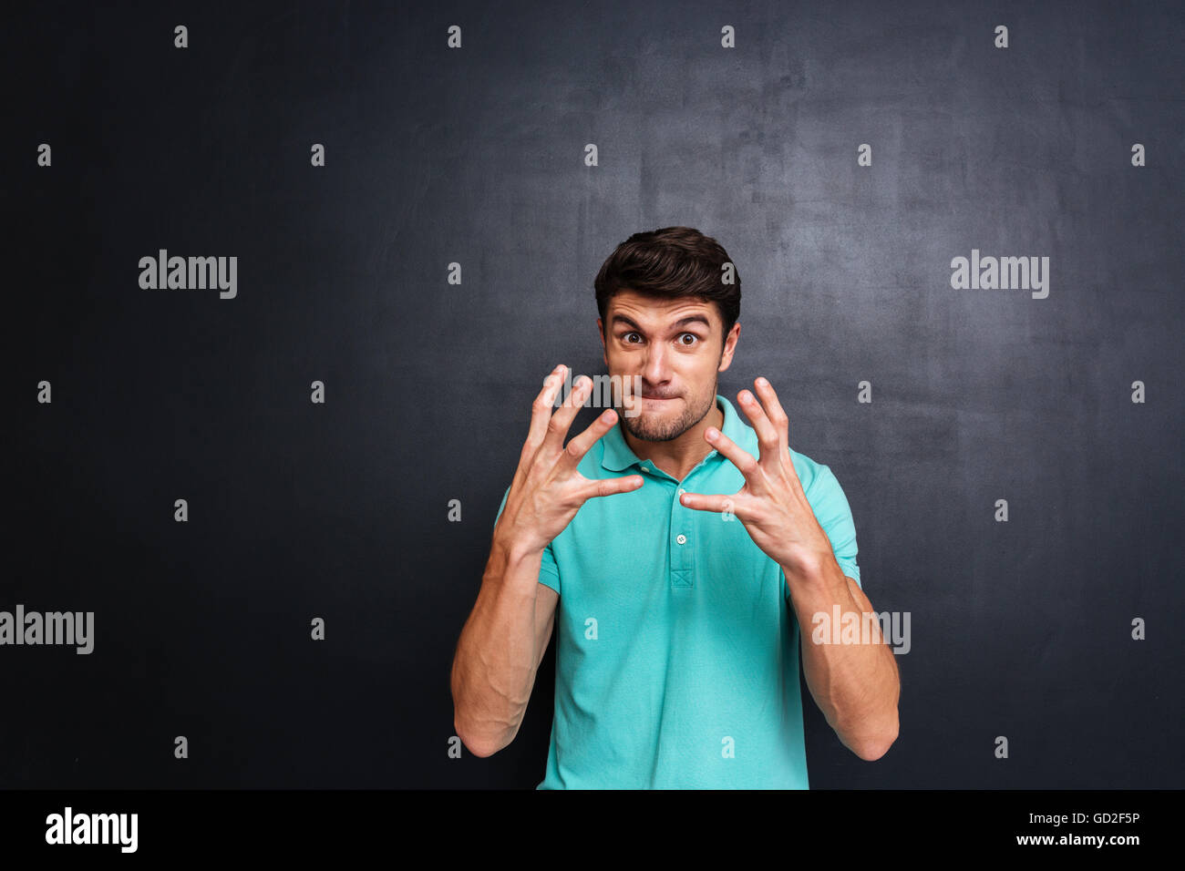 Wütend irritiert junger Mann im blauen T-shirt über Tafel Hintergrund Stockfoto