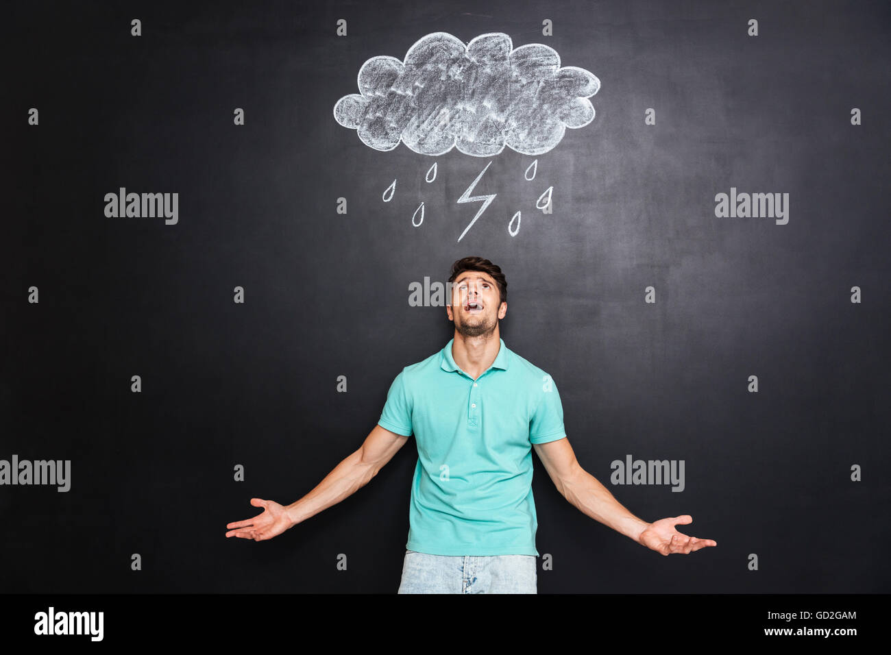 Zorniger junger Mann stehend mit erhobenen Händen und rief über Tafel mit gezeichneten Regenwolke Stockfoto
