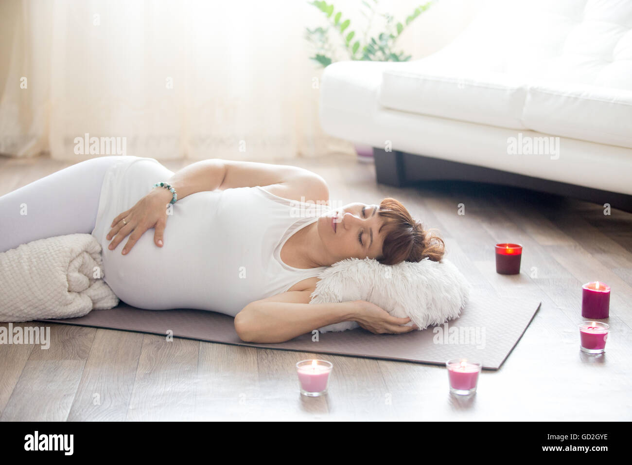Gesunder Lifestyle-Konzept. Schwangerschaft-Yoga und Fitness. Junge schwangere Yoga Frau ruht nach einem Training im Wohnzimmer Stockfoto