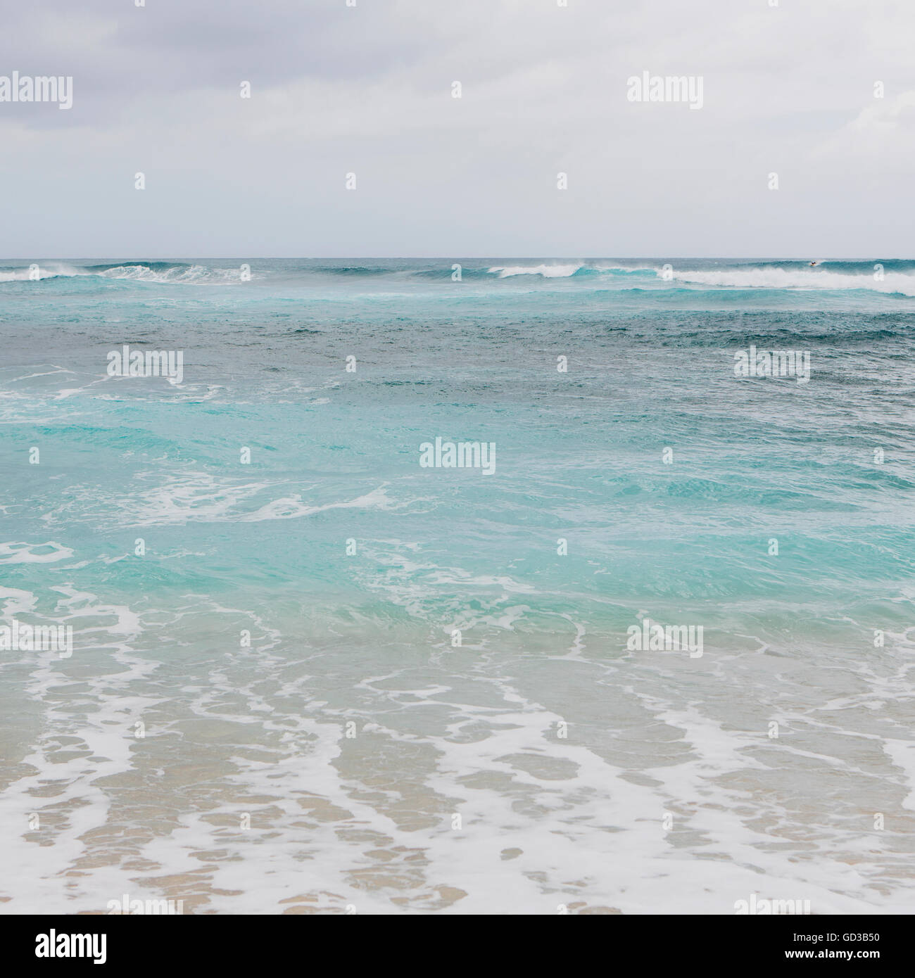Türkisblaue Meerwasser, Wellen am Strand und bedecktem Himmel. Stockfoto