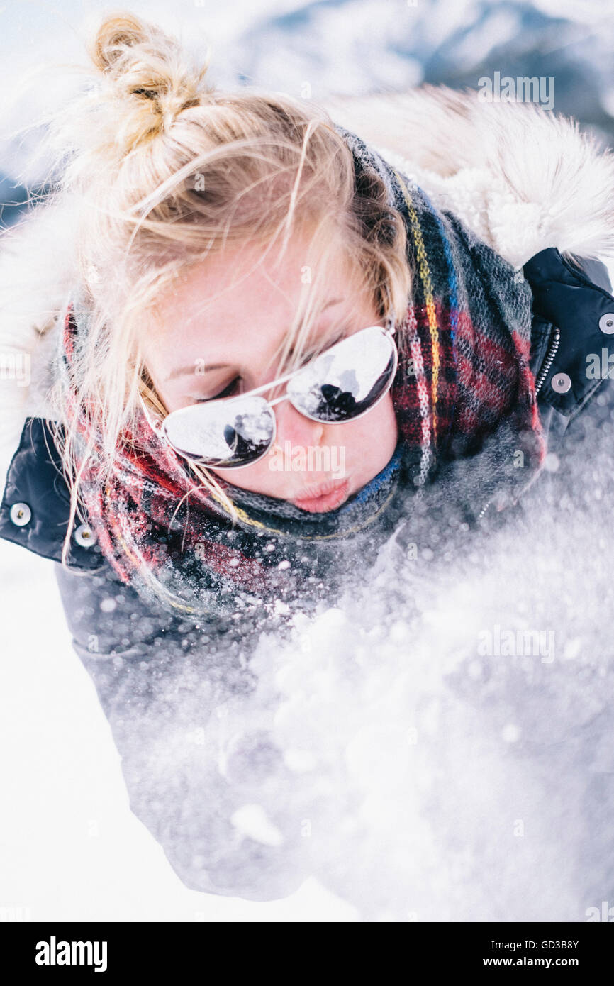 Eine junge Frau mit Sonnenbrille weht frischen Schnee aus ihren Händen. Stockfoto