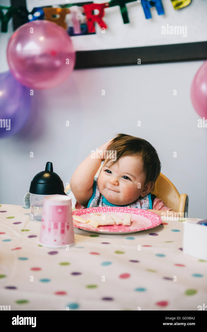 Ein Kind, ein einjähriges Mädchen auf ihrer Geburtstagsparty, in einen Hochstuhl an einem Tisch sitzen. Stockfoto