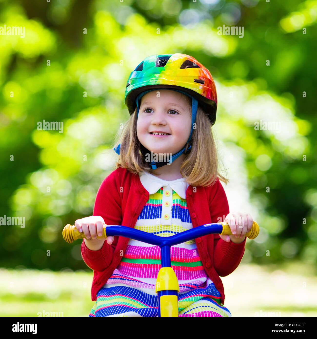 Niedliche Mädchen reiten ihr Dreirad im sonnigen Sommerpark-Schutzhelm tragen. Kinder Fahrrad. Erstes Fahrrad für kleines Kind. Stockfoto