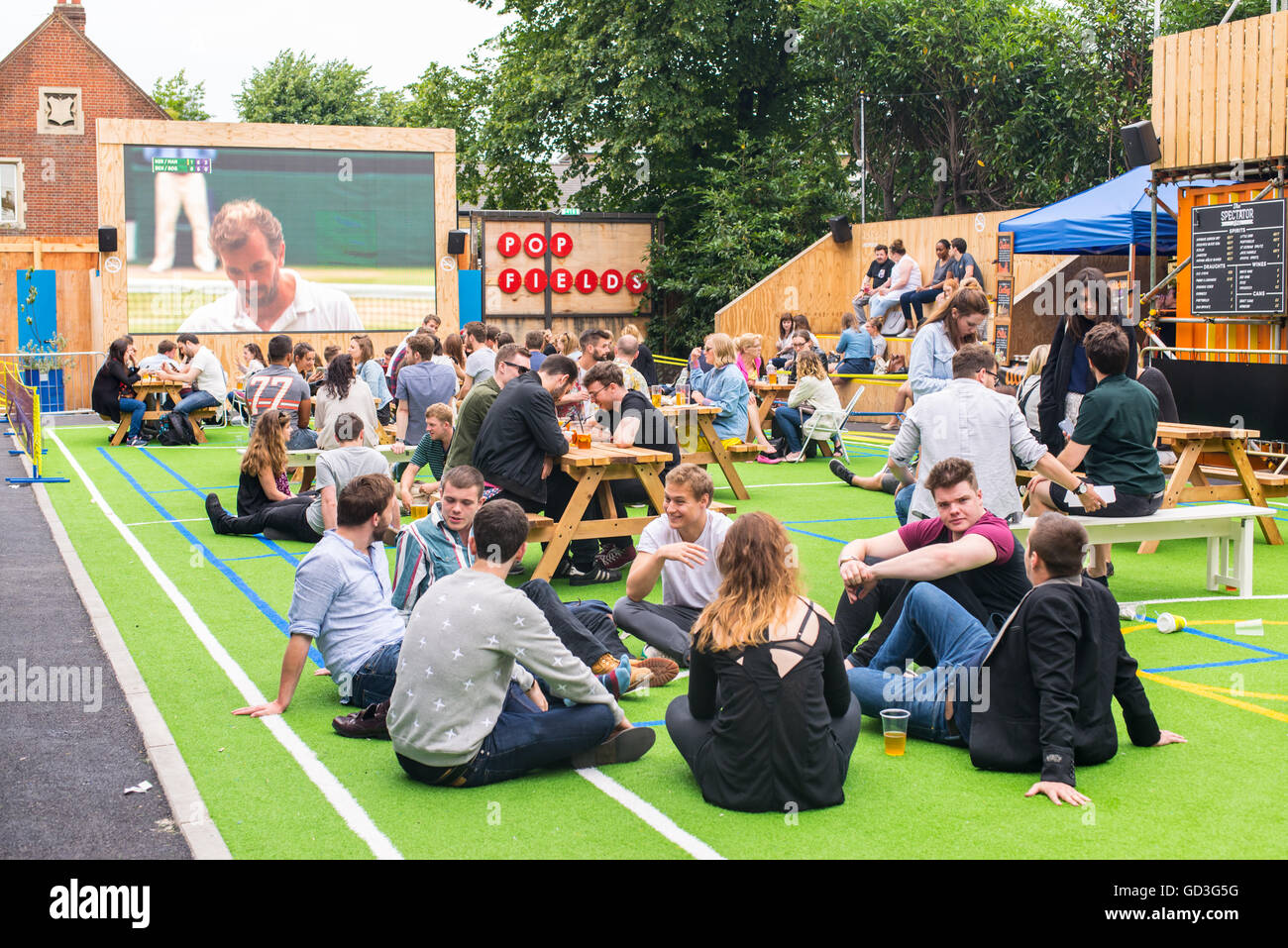 Die Menschen reden und trinken während Sie Wimbledon Tennis Match in einem großen draußenen Bildschirm in pop Felder, brixton Stockfoto