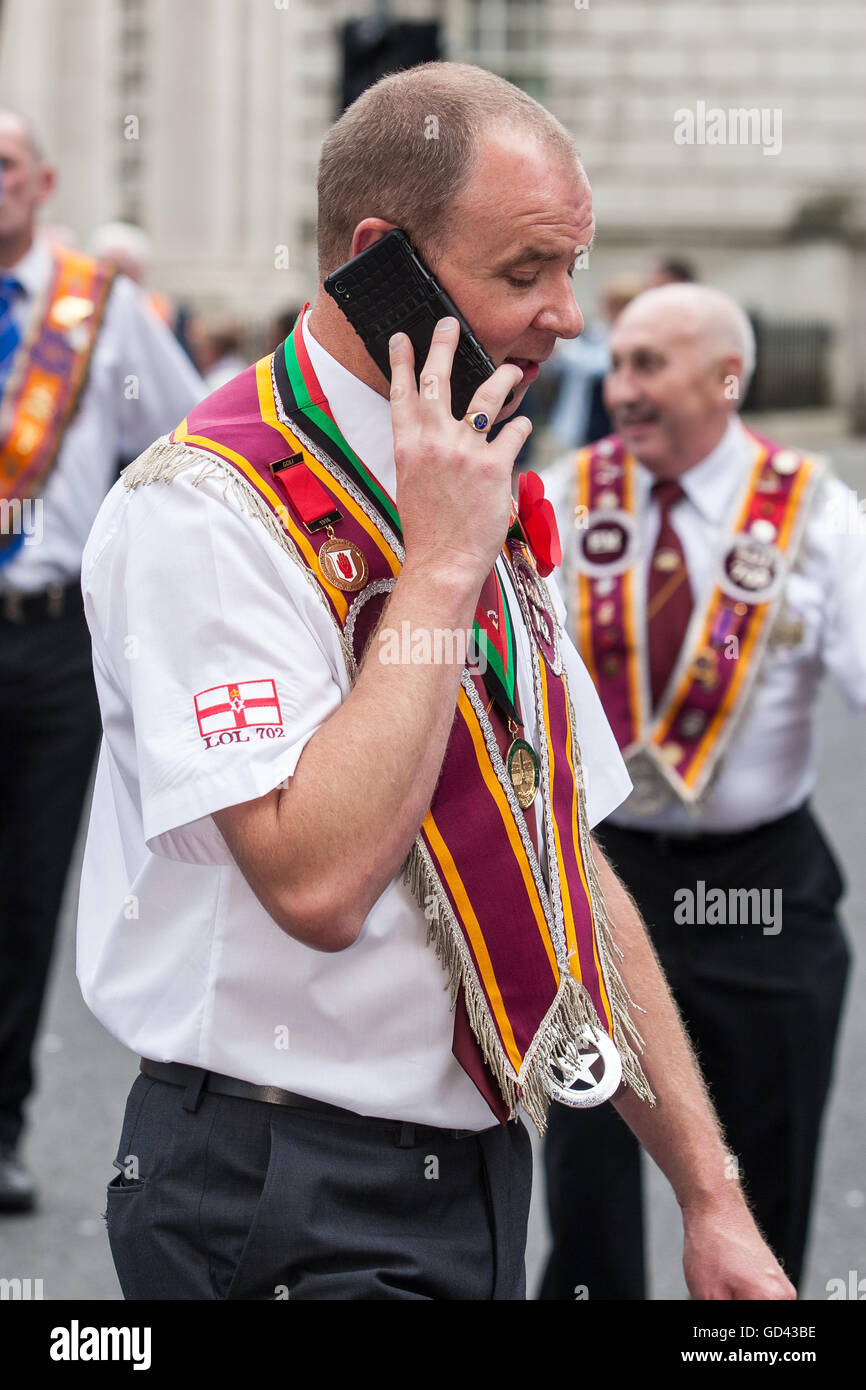 Belfast, UK. 12. Juli 2016. Ein Mann auf seinem Handy nach der Prozession von Demonstranten gestoppt während der 12. März. Es entstand während des späten 18. Jahrhunderts in Ulster. Es feiert die Glorious Revolution (1688) und der Sieg des protestantischen Königs Wilhelm von Oranien über katholische König James II an Schlacht des Boyne (1690) Credit: Bonzo/Alamy Live News Stockfoto