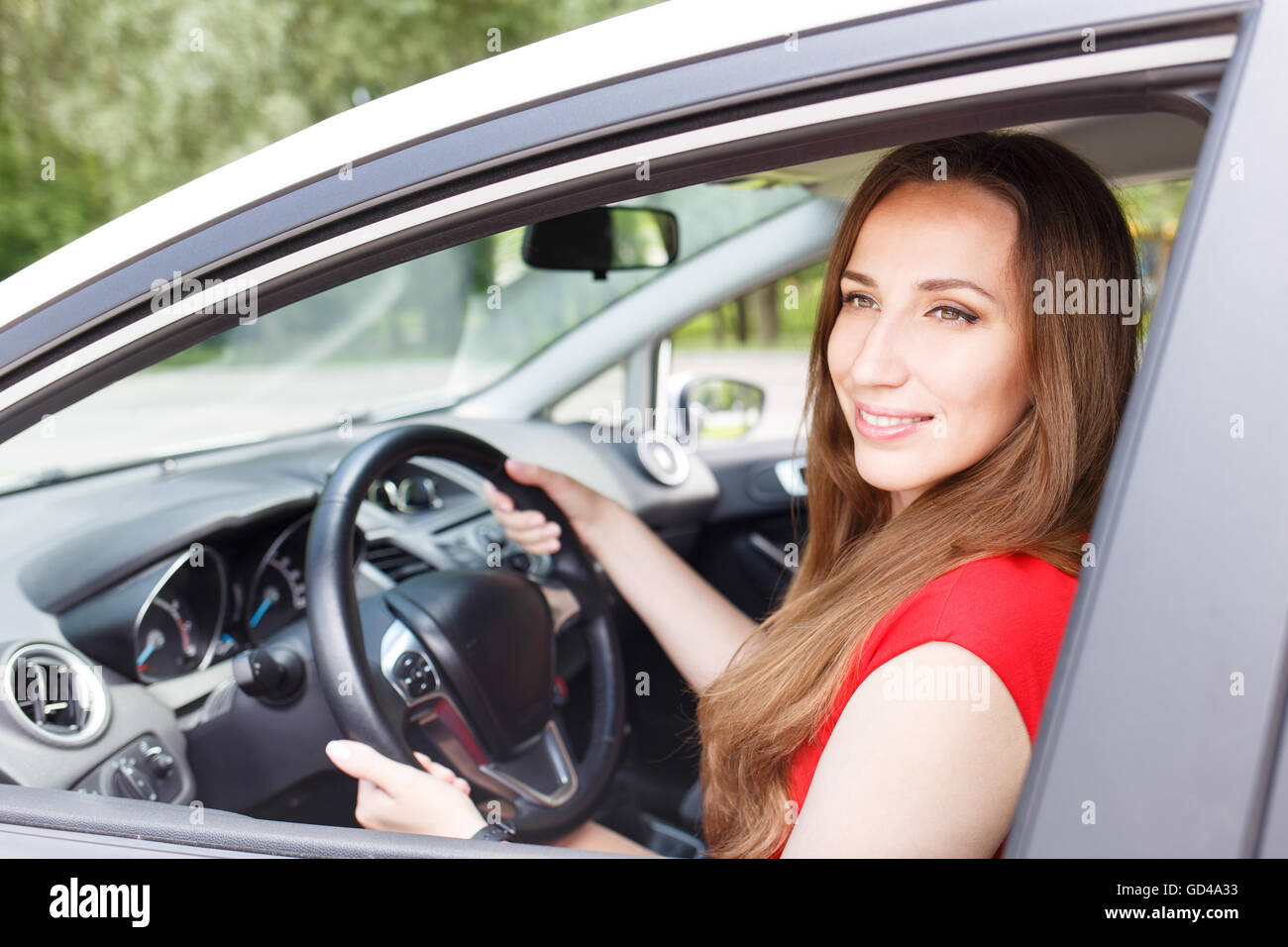 Junge schöne Frau-Lenkrad, ein Auto zu fahren. Zuversichtlich lächelnden Dame im roten Kleid, ein Auto zu fahren Stockfoto