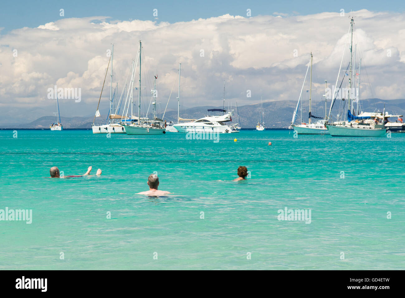 Urlauber entspannen in dem klaren, türkisfarbenen Meer bei Lakka, Paxos - Blick auf Luxus-Boote ankern vor der Küste Stockfoto