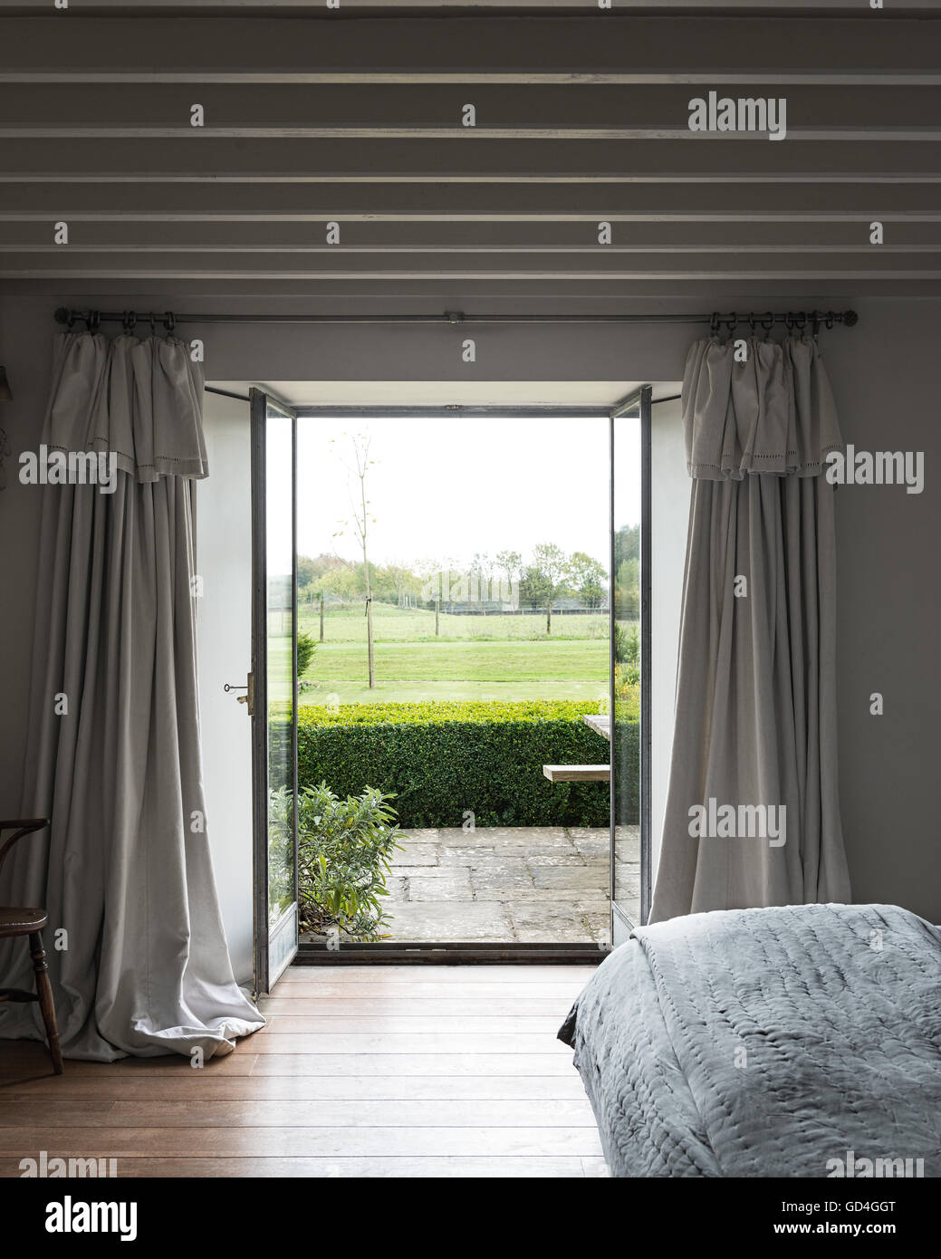 Blick durch offene Glastür mit Französisch Leinenvorhängen durch steinerne Terrasse und Garten Stockfoto