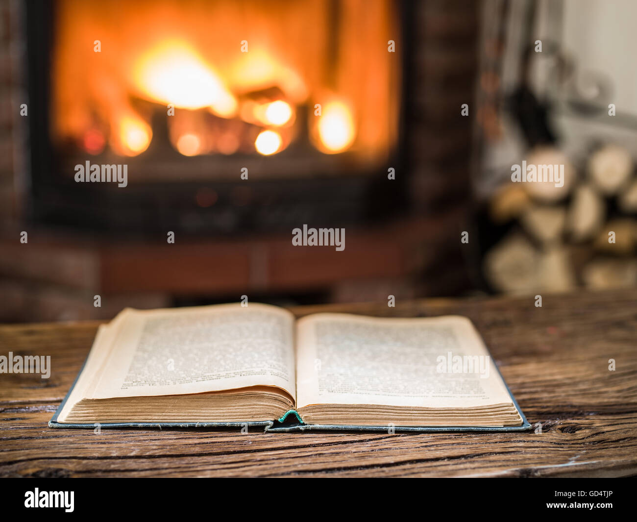 Aufgeschlagenes Buch auf dem Holztisch. Kamin mit warmen Feuer im Hintergrund. Stockfoto