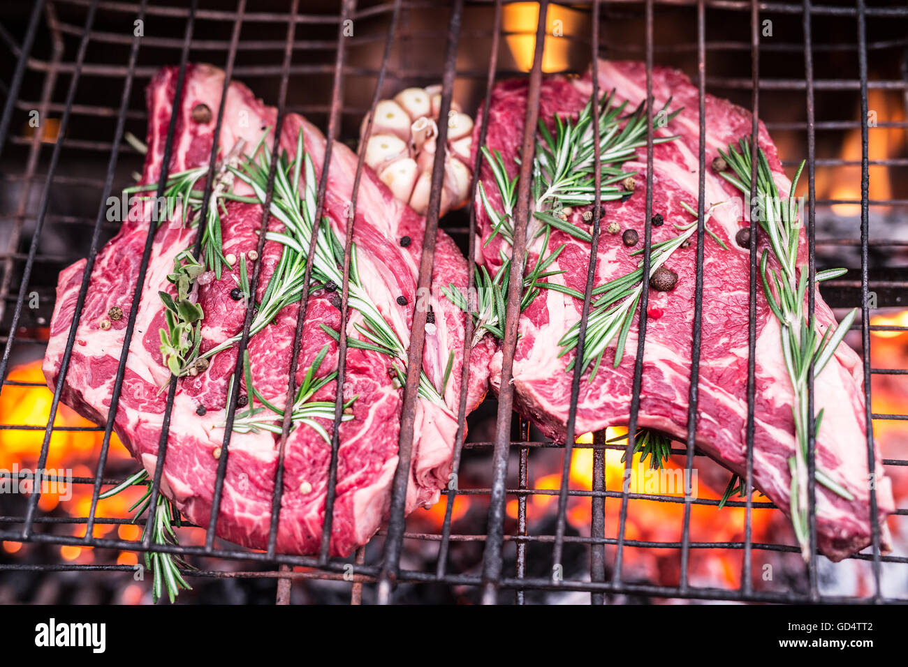 Rib-Eye-Steaks und Grill mit brennendem Feuer hinter ihnen. Stockfoto