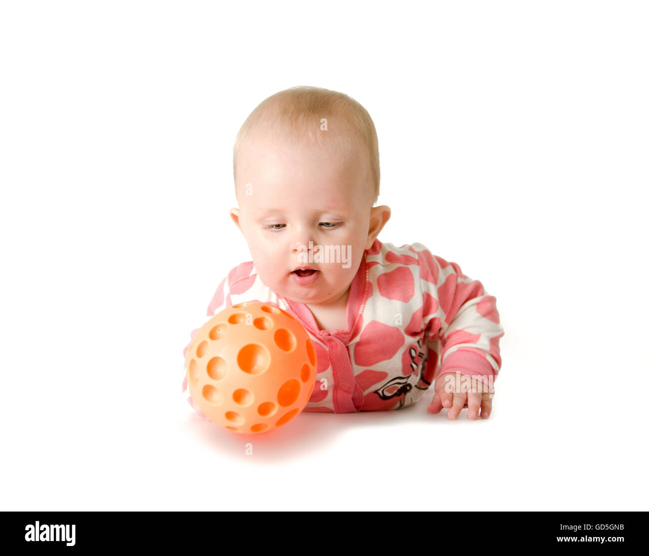 Kleine Mädchen tragen weiße und rosa Pyjama, rote Socken spielt mit ihren orange Ball liegend auf dem Bauch Stockfoto