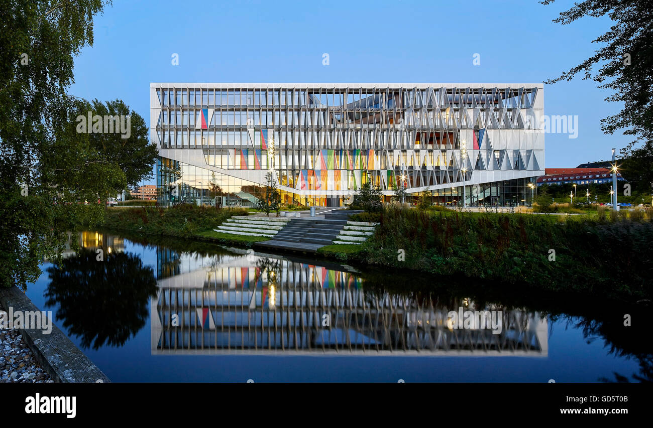 Abenddämmerung Höhe des Gebäudes mit Spiegelbild im Fluss. SDU Campus Kolding, Kolding, Dänemark. Architekt: Henning Larsen Architects, 2015. Stockfoto