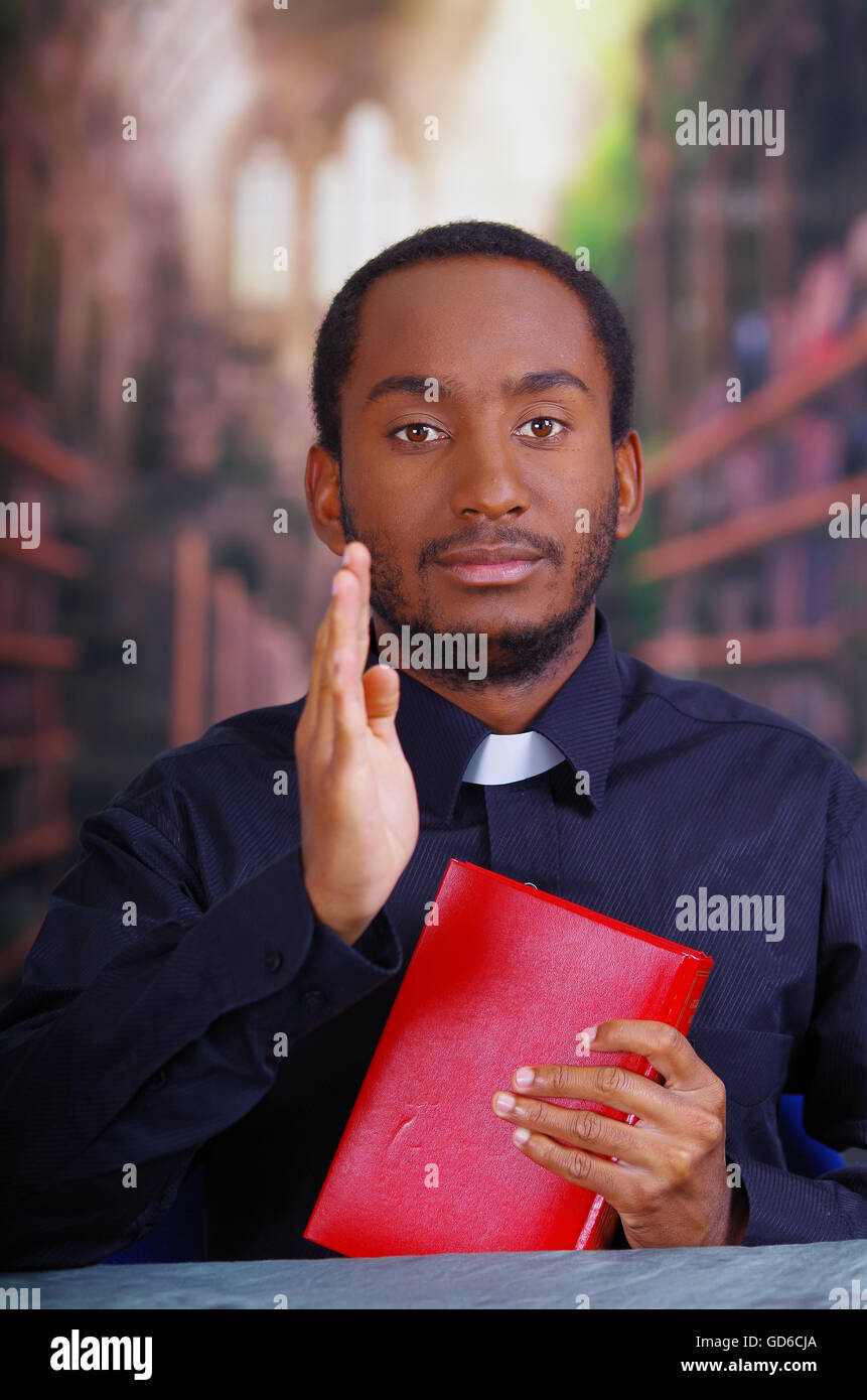 Katholischer Priester tragen traditionelle Clerical Collar Shirt sitzen und Holding Bibel in Kamera, Religion-Konzept Stockfoto