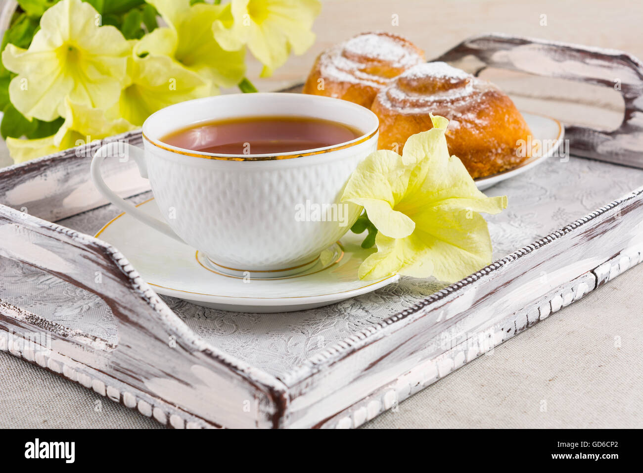 Frühstück Plundergebäck und Tasse Tee auf Vintage Serviertablett. Süße Zimtschnecken und Teetasse mit gelben Blüten. Frühstück Stockfoto